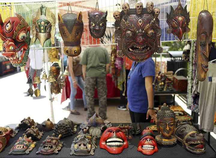 Anima Budhathoki waits for customers behind a display of wooden masks from Nepal at the booth for Sanùs Nepali Bazaar at the temporarily relocated Pearl Market on the Statehouse grounds.  (Jonathan Quilter / The Columbus Dispatch)